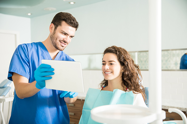 Dentist Showing Digital Tablet To Female Patient In Clinic