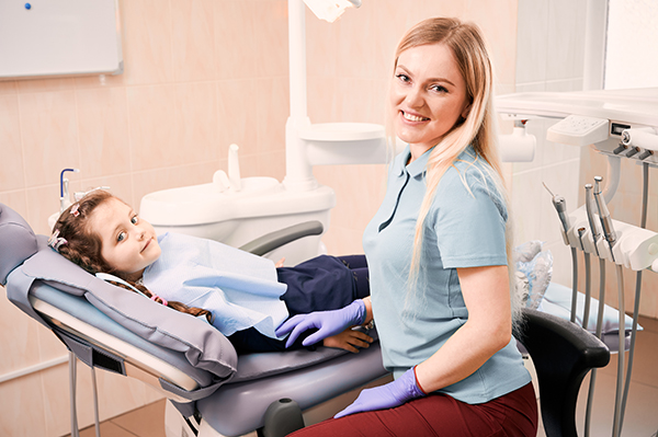 Pediatric dentist sitting beside adorable little girl in dental office.